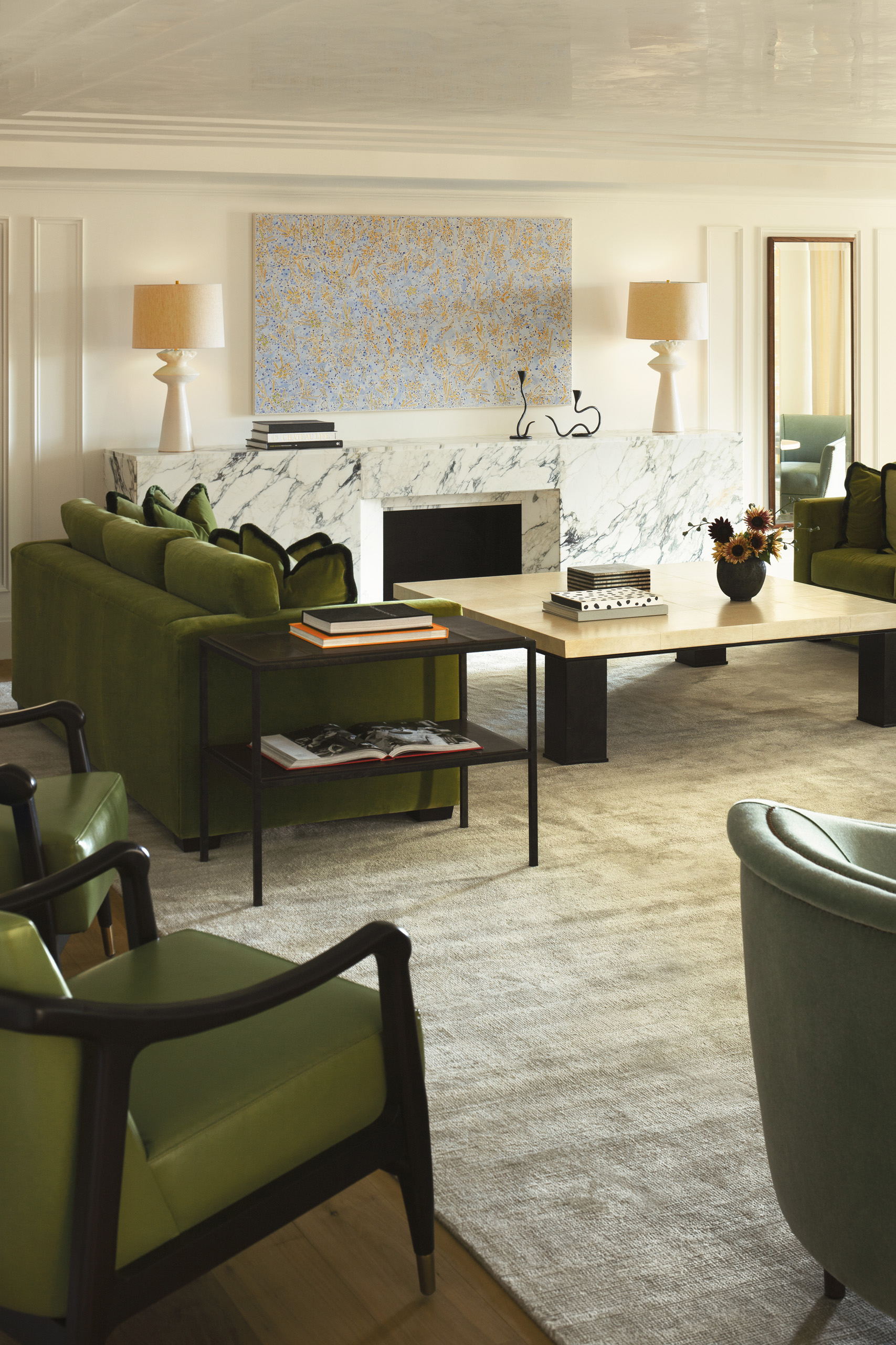 Wide living room with marble fireplace and green sofas.