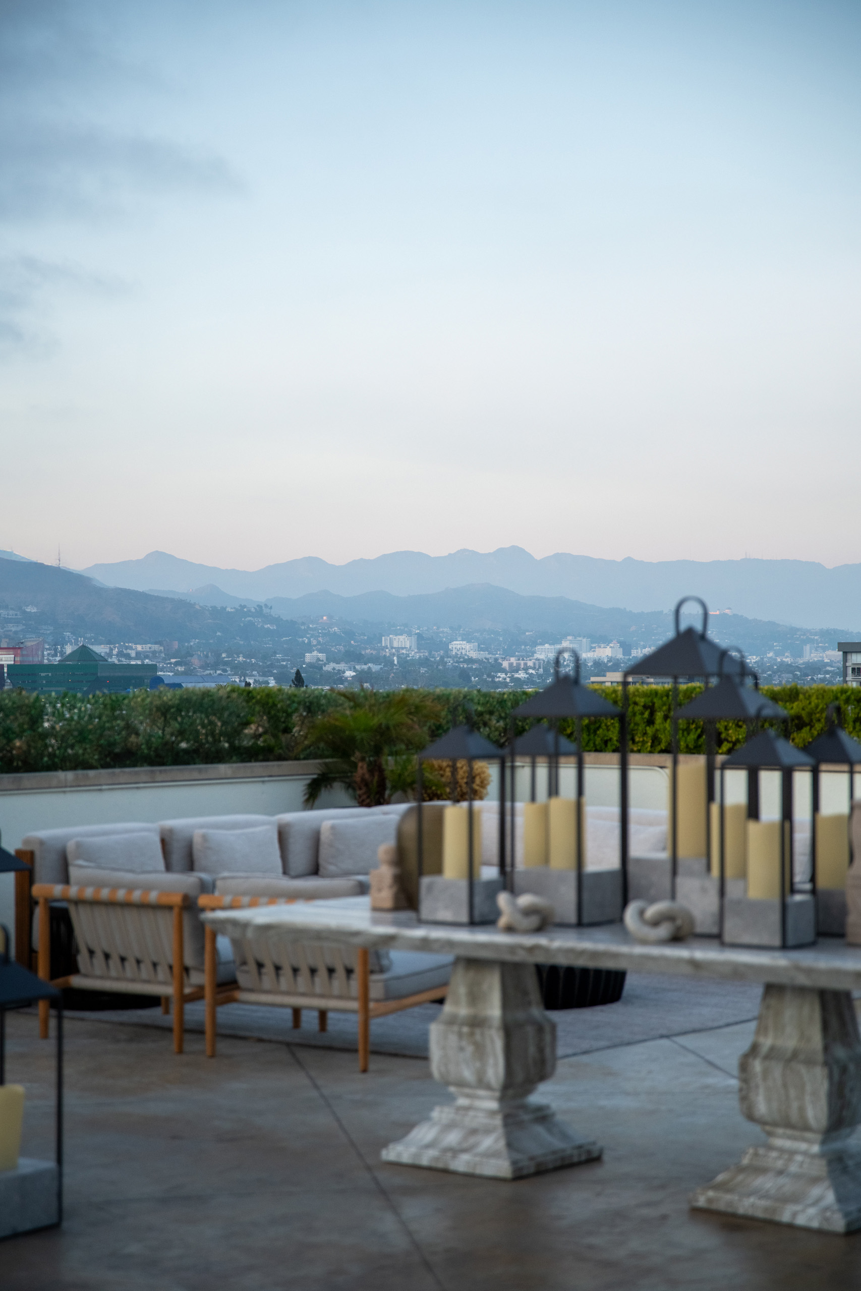 Rooftop lounge at dusk with lanterns in the foreground and distant mountain views.