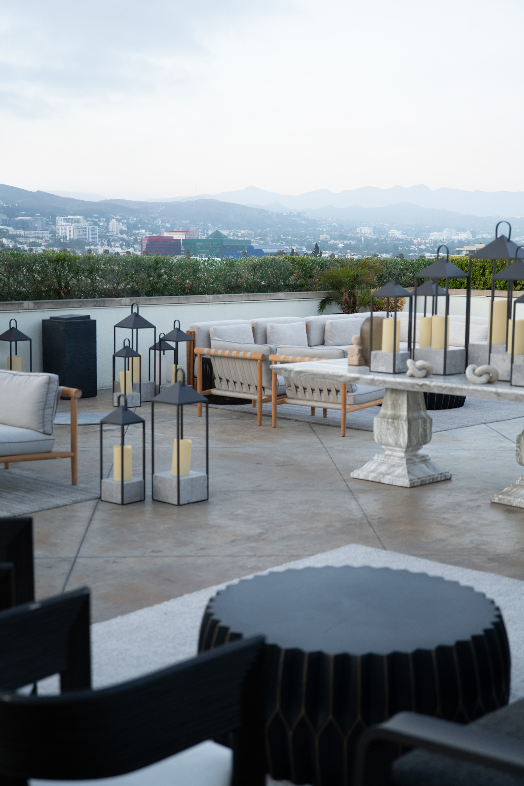 Rooftop terrace with lanterns and modern lounge seating overlooking a hazy hillside skyline.