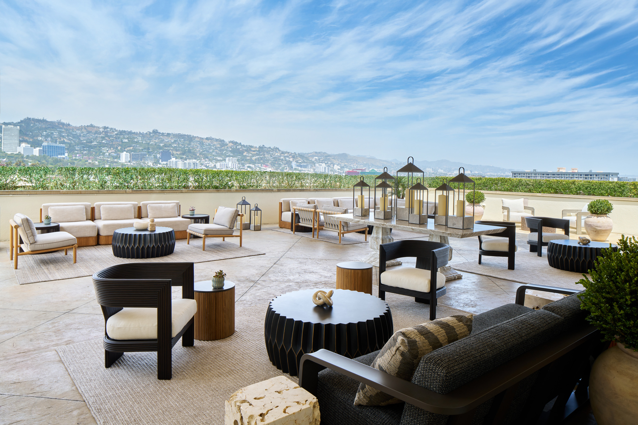 Panoramic rooftop terrace with lounge seating, lanterns, and hillside views under a blue sky.