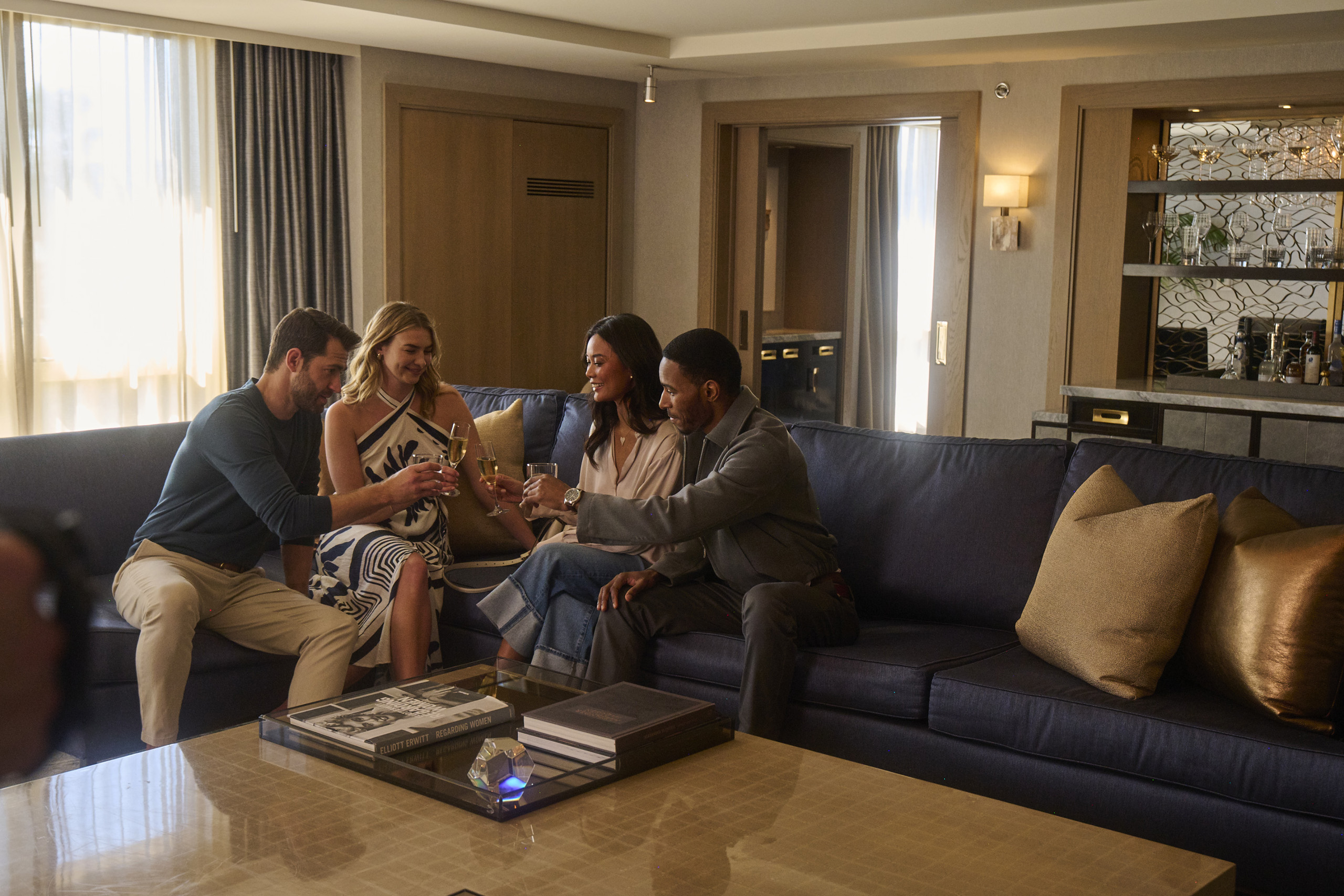 Friends toast champagne on sofa in stylish suite.