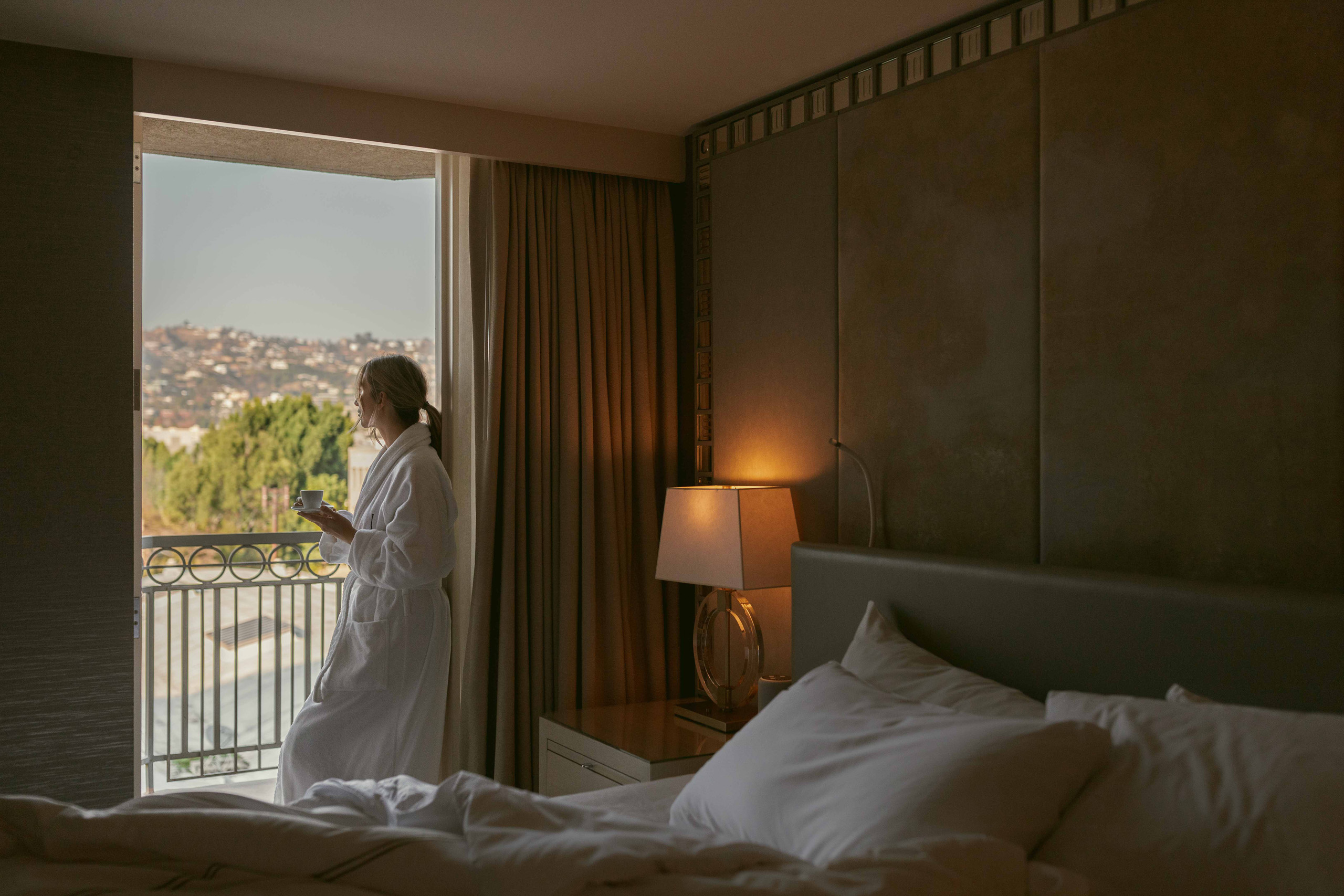 Woman in robe holding coffee by balcony window