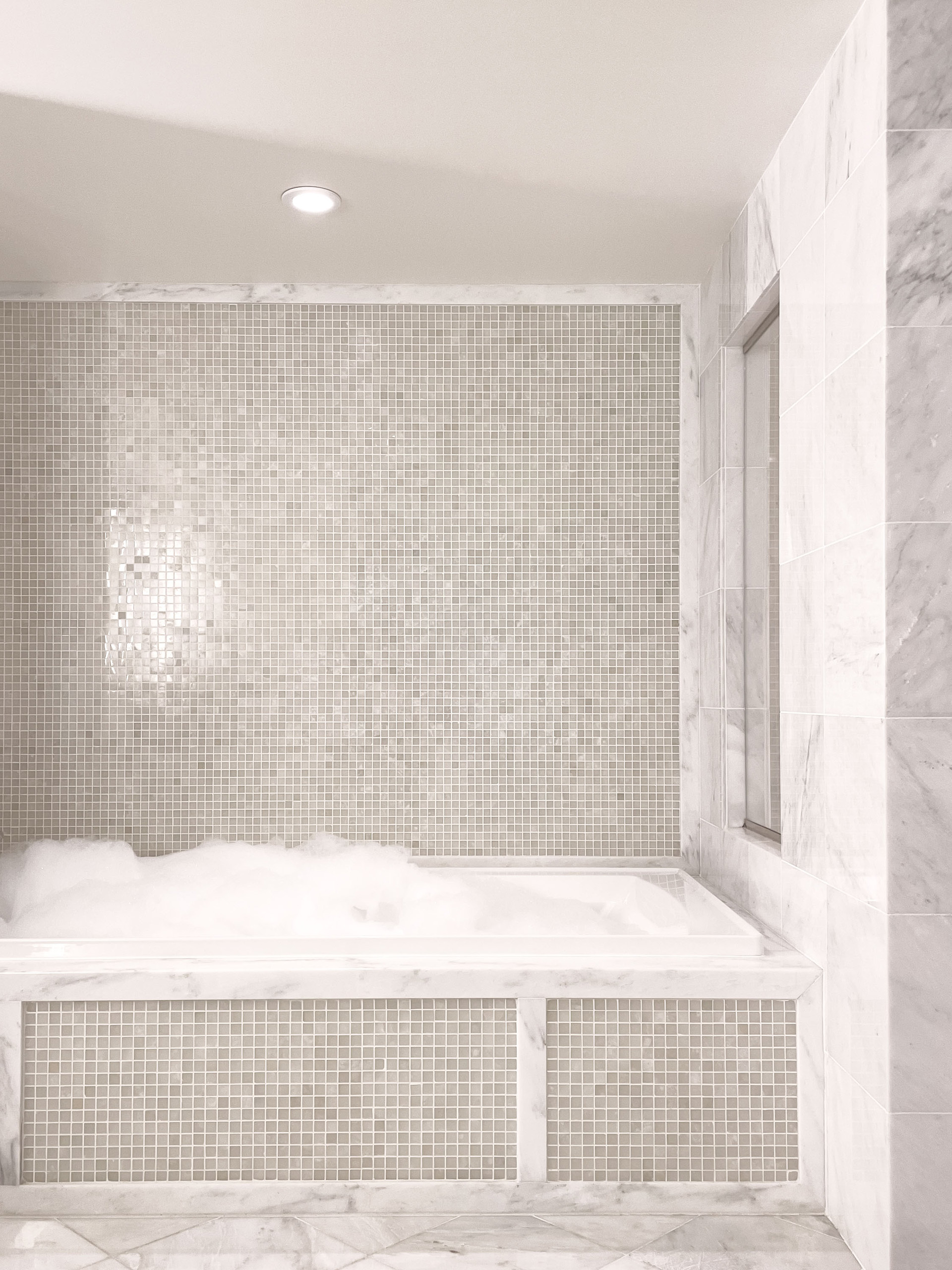 Bubble-filled marble tub with mosaic tile surround.