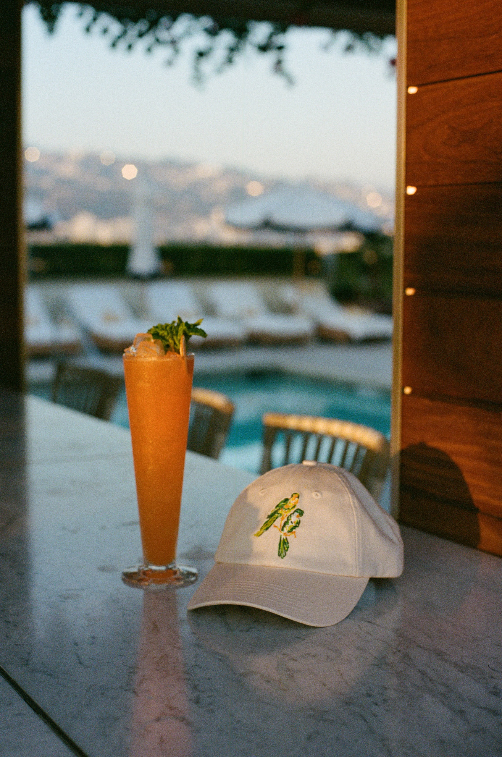 White cap beside orange cocktail at rooftop bar