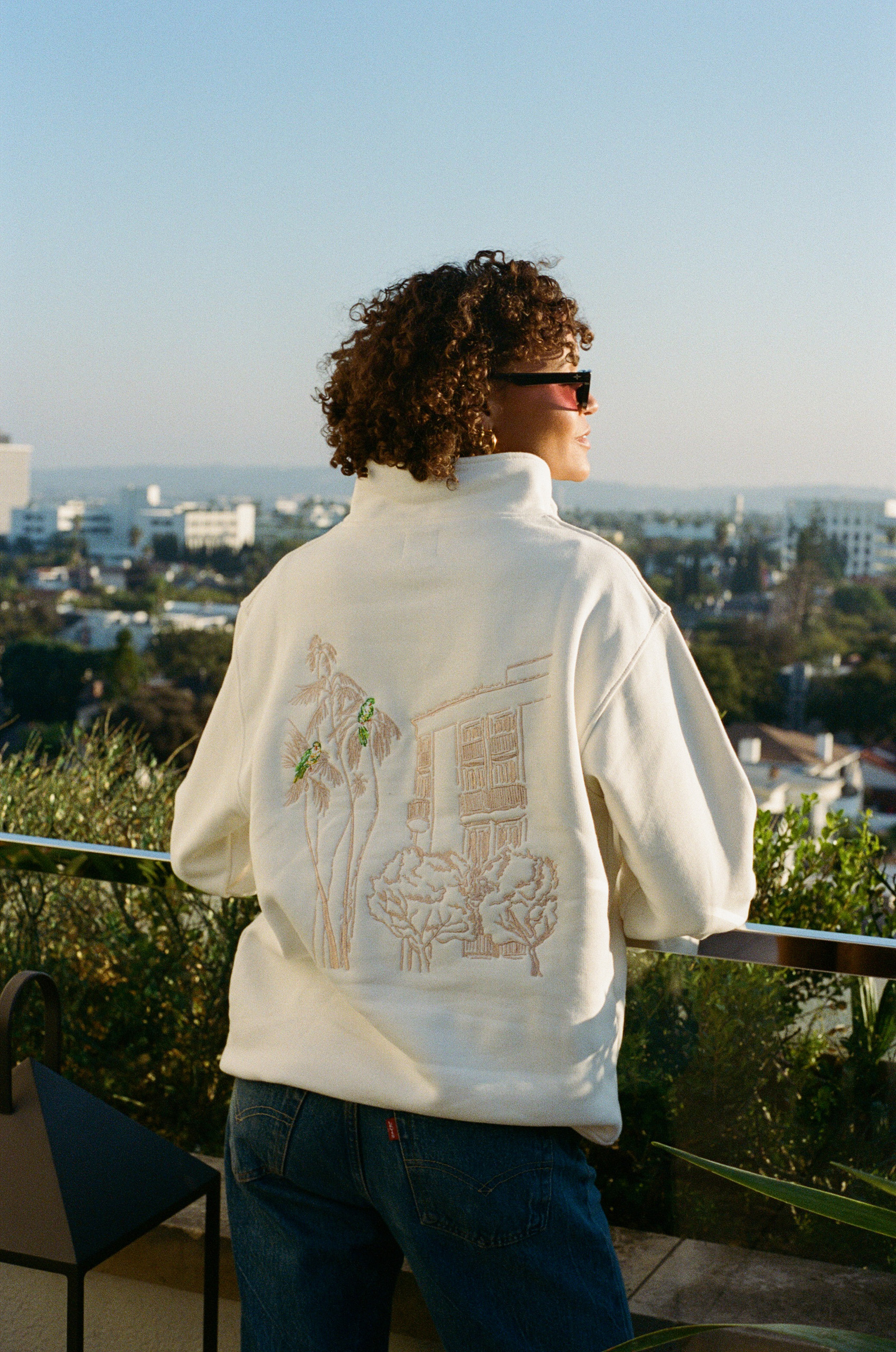Guest in embroidered pullover overlooking city skyline.