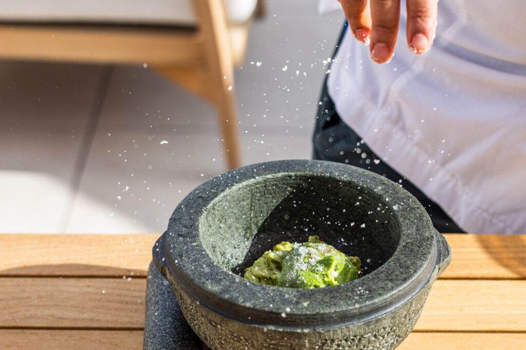 Hand sprinkling salt into fresh guacamole in stone bowl