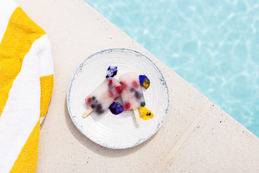 Fruit popsicles on plate beside sparkling pool water