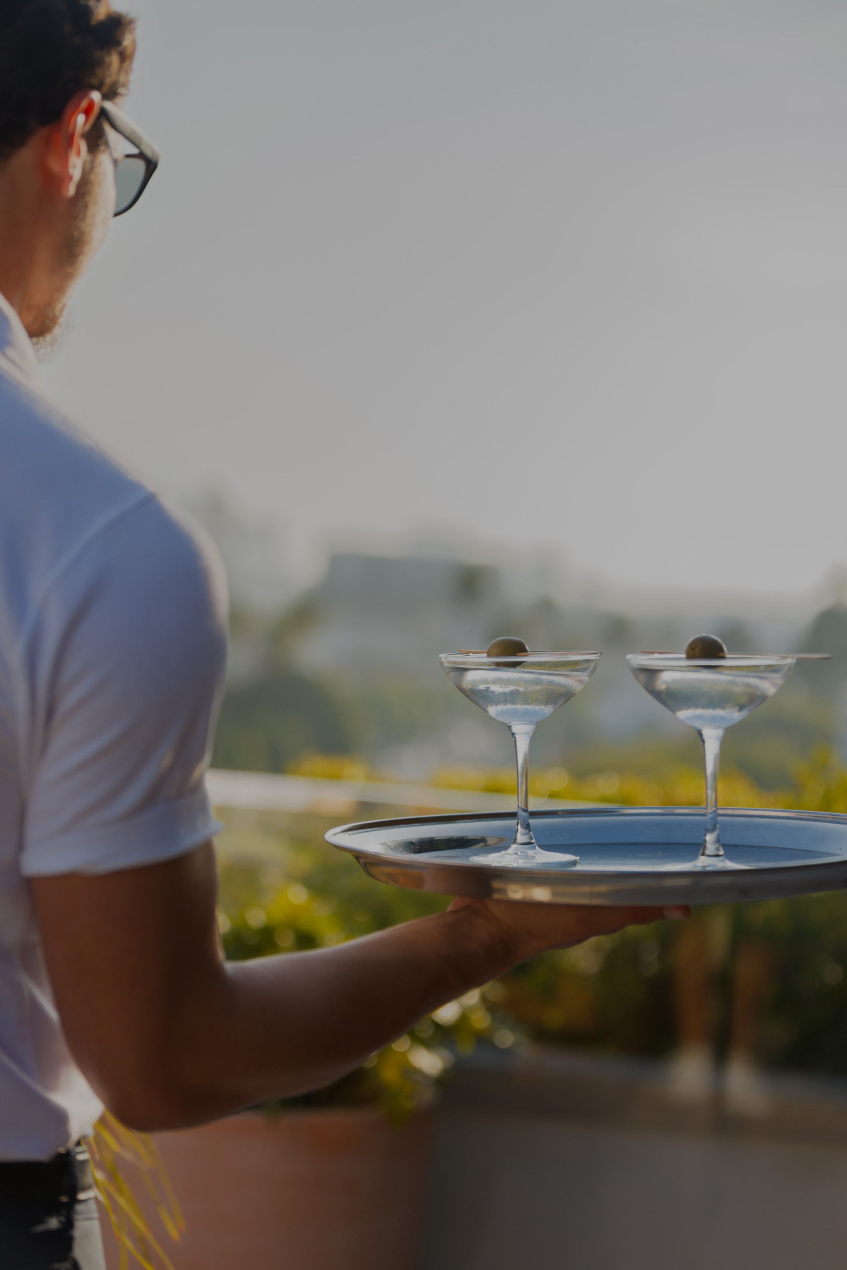 Server carrying two martinis on tray at sunset