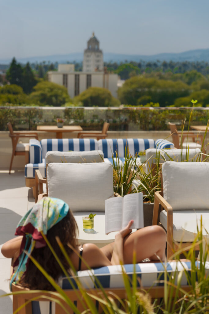 Woman reading by rooftop pool with city view.