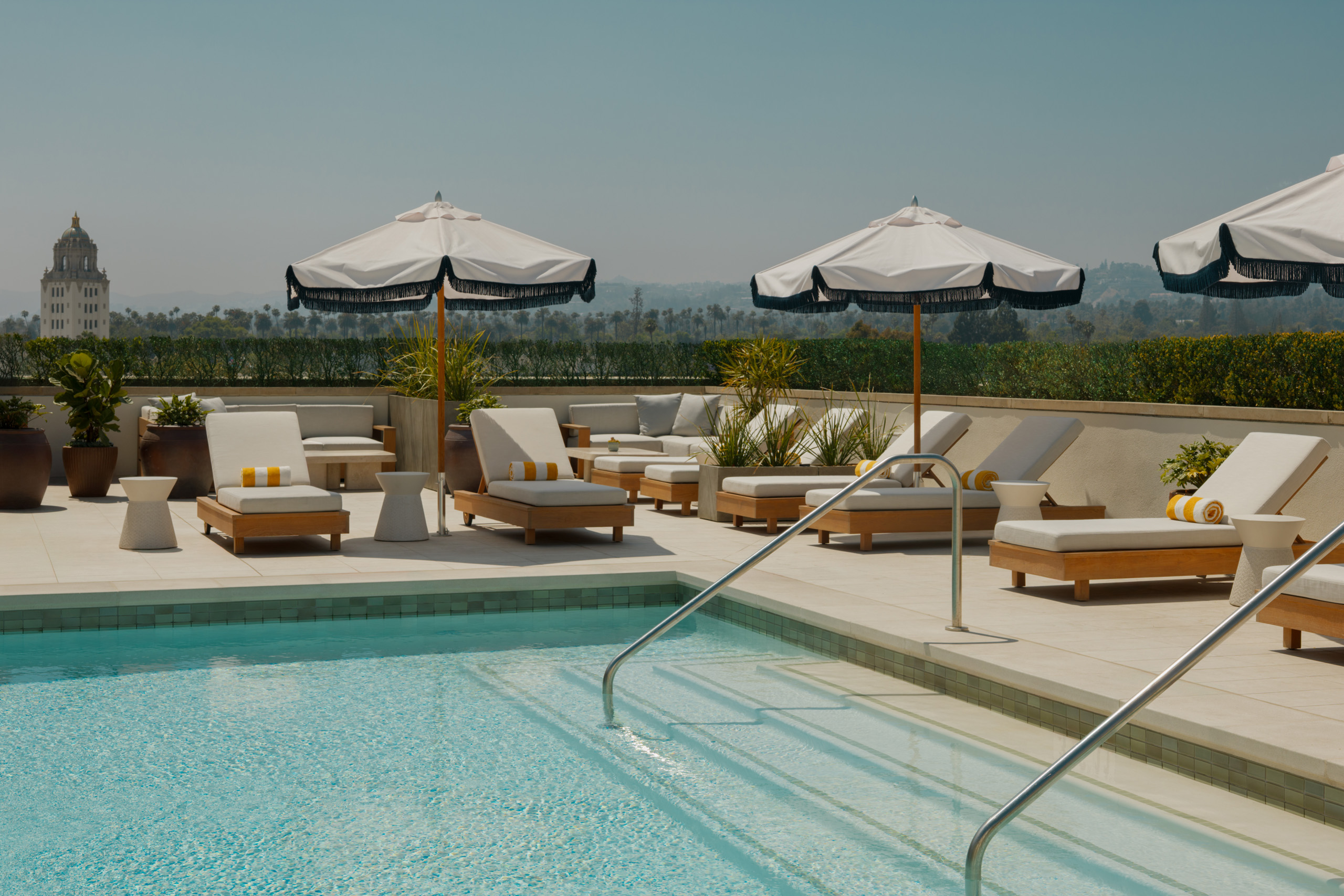 Rooftop pool with umbrellas and distant Beverly Hills view.