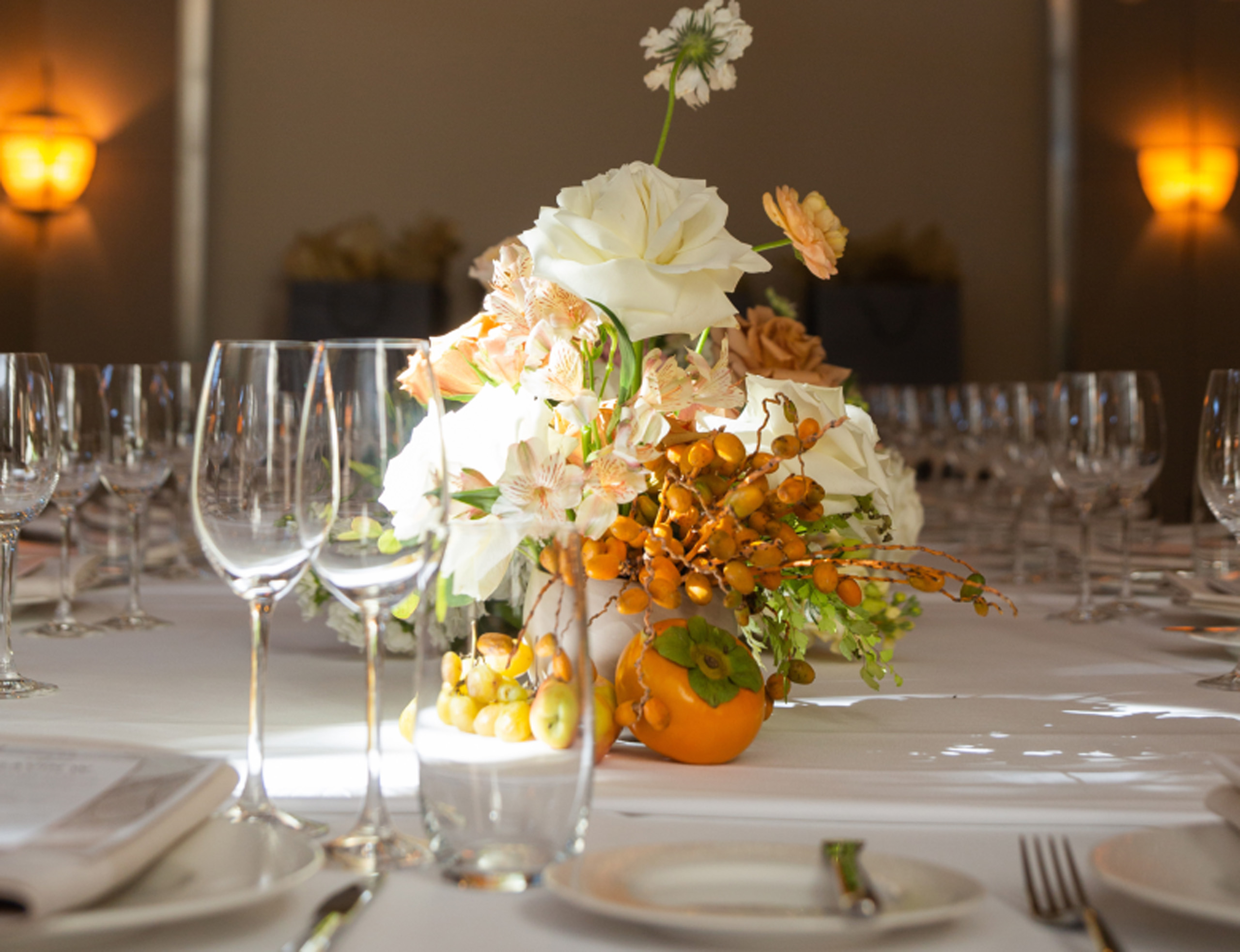 Floral centerpiece with fruit on elegantly set table.