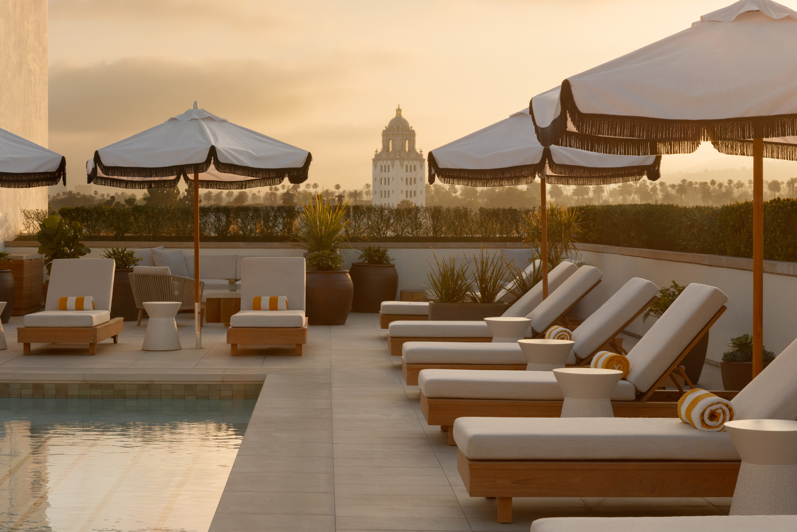 Rooftop pool loungers and umbrellas at golden sunset.