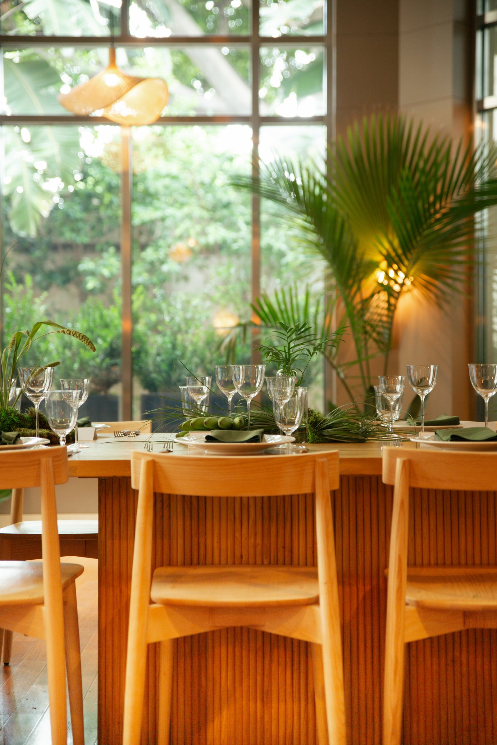 Elegantly set dining table in L'Ermitage Beverly Hills' Rotunda event space, featuring crystal glassware, green botanical centerpieces, and warm natural light through floor-to-ceiling windows