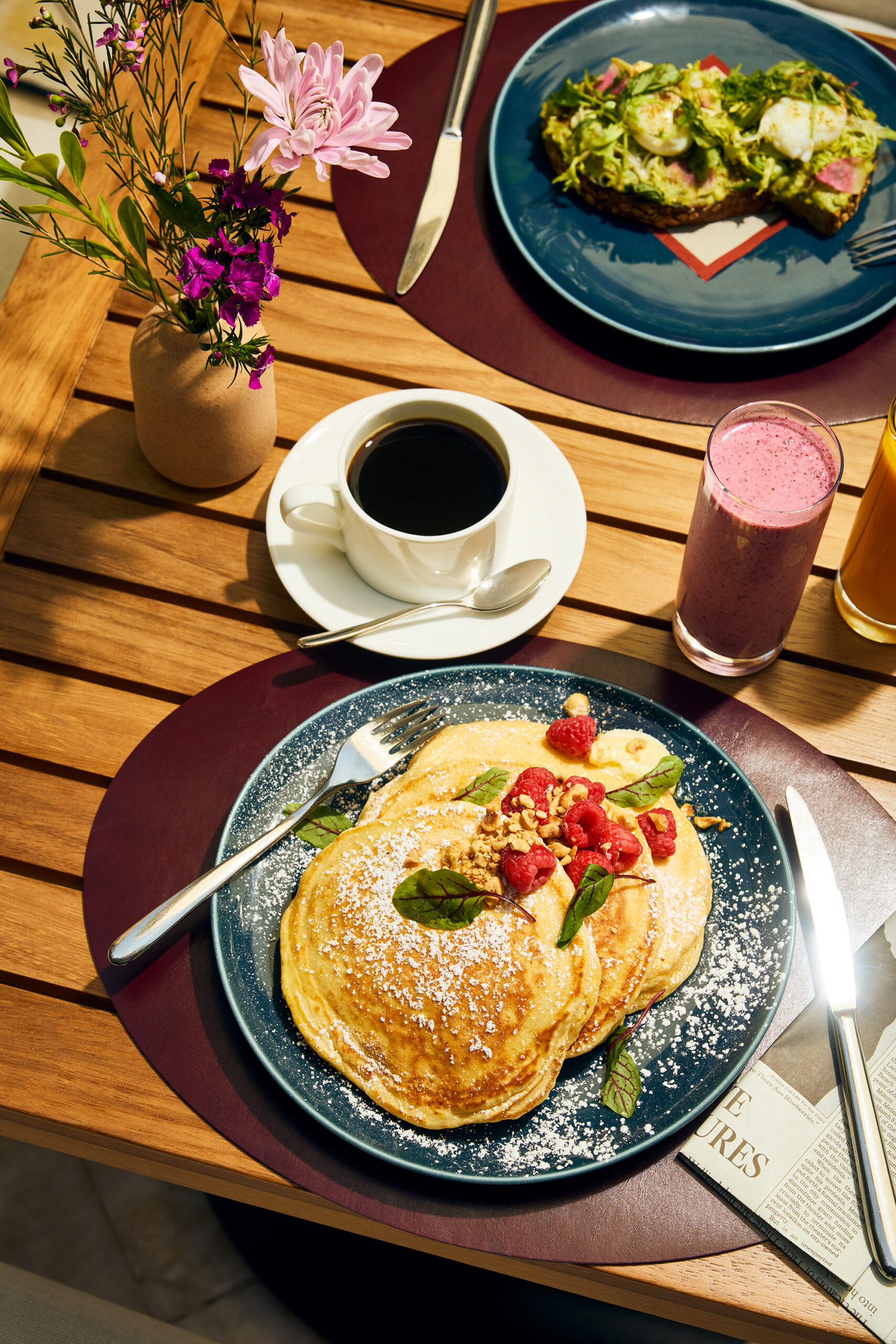 Breakfast spread with pancakes, coffee, smoothies, and newspaper on a wooden table