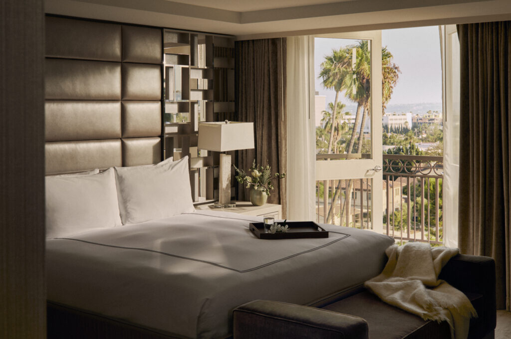 a white bed in a naturally sunlit hotel room with palm trees outside the window